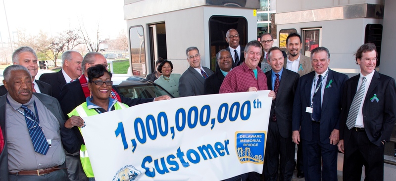 Delaware Memorial Bridge milestone: Jeff Wright of Wildwood, New Jersey, was the one billionth customer at the Delaware Memorial Bridge. Delaware Memorial Bridge toll collector Loretta Overton (left) joins with Jeff (right) to hold the ceremonial banner in Lane 2 of the Toll Plaza. Delaware Governor Jack Markell (next to Mr. Wright) presented the honoree with a framed commemorative photo of the Delaware Memorial Bridge; a copy of Bill Miller’s “Crossing the Delaware”, a book that chronicles the history of the Delaware Memorial Bridge; and a souvenir silver Bridge token. To the right of Governor Markell are Commission Vice Chairman Jim Hogan and Chairman Bill Lowe. BY DRBA