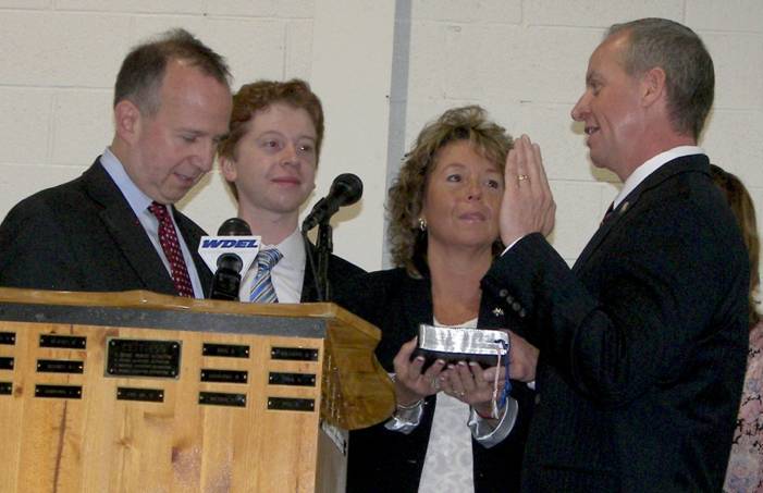 Robert M. Coupe, right, takes the oath of office as he is sworn in by Gov. Jack Markell, left, as commissioner of the Delaware Department of Correction. Coupe’s wife, Pamela, is holding a Bible, while their son, Tyler, looks on. Coupe’s daughter, Jocelyn, is standing behind him on the stage. SOURCE SUBMITTED