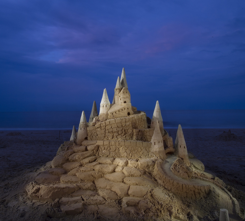 The Community Sandcastle build led by professional sandcastle builder Darrell O’Connor takes on a mysterious glow at dusk. BY DENY HOWETH