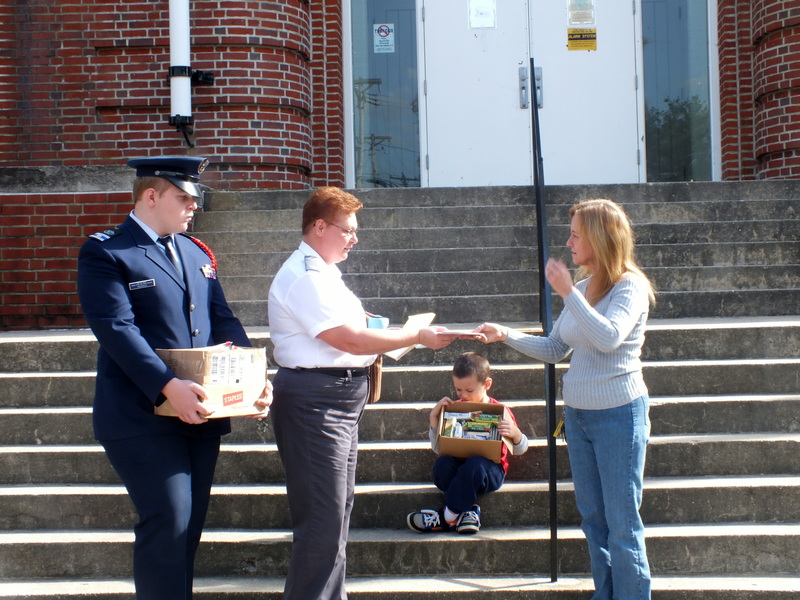 Shown (l-r) Cadet 2nd Lt. Tyler Marker and Lt. Virginia Marker of Coastal Patrol Base 2 Memorial Composite Squadron present thank-you expressions to its squadron liaison, Kim Rogers, mother of a Guardsman now deployed in Afghanistan. Seated, young Clifford Reed holds one of the Love Boxes which the group assembled for the deployed unit, which is based at Georgetown. SOURCE SUBMITTED