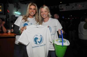 Delaware Coast Aid committee members Julie Wyatt, left, and Laura Olenderski keep busy raising funds by selling event T-shirts. BY STEVEN BILLUPS