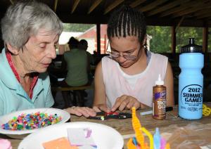 Volunteer Barbara Spence, left, assists Antonia Harris in making a mask during arts and crafts time. BY DAN COOK