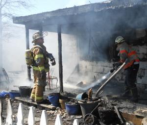 A Delaware State Fire Marshal soaks hot debris on the porch of the house while a member of the Lewes fire department stands watch. BY CHRIS FLOOD