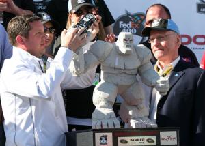 Gary Camp, director of public relations at Dover International Speedway, places the winning car of Jimmie Johnson in the hand of the Miles the Monster Trophy. BY PAT IRELAN