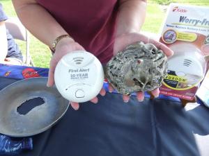 Rebekah Legar of the Office of the State Fire Marshal holds a new smoke detector next to a smoke detector that survived a fire. Legar said while it won't be used again, the burnt smoke alarm still works. BY TAGGART HOUCK