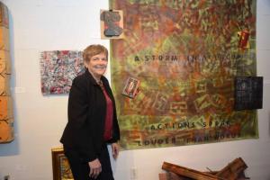 Rose Minetti stands with several different Arte Provera pieces. The large piece is titled “Storm in a Teacup.” It is made up of a shower curtain, spraypaint, stencils, cardboard and packing materials. RAL assemblage