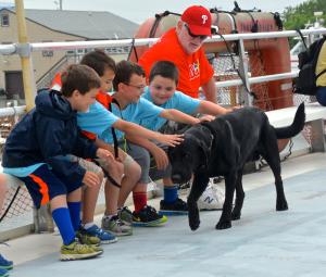 Who can resist petting a friendly dog? Surely not this group of first-graders who are (l-r) Dalen Daminger, Anthony Rodriguez, Jake Hutchison, Patrick Donahue and his grandfather, John Donahue. They are petting Capt. H.D. Parson's dog Magic. BY RON MACARTHUR