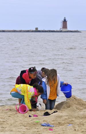 A group of Richard Shields kindergarten students dig in the sand with the Harbor of Refuge Lighthouse in the background. BY RON MACARTHUR