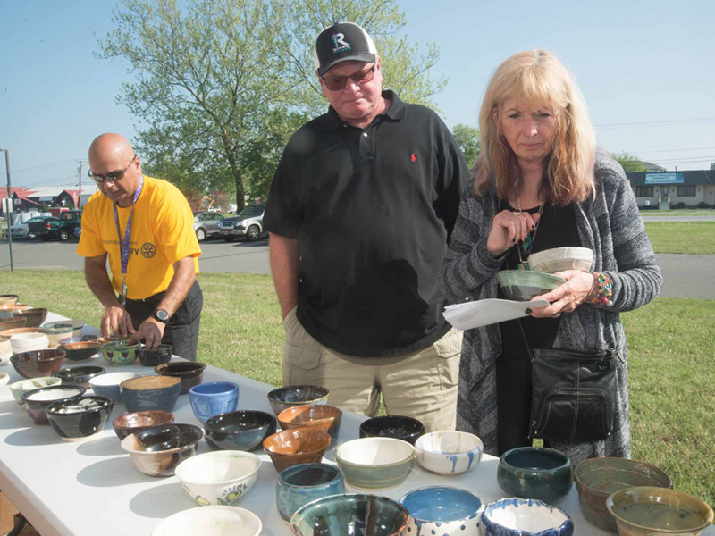 Roy Peacock and Norma Davall from Lewes browse the bowls as Dr. Uday Jani, pottery committee chair, arranges the bowls.