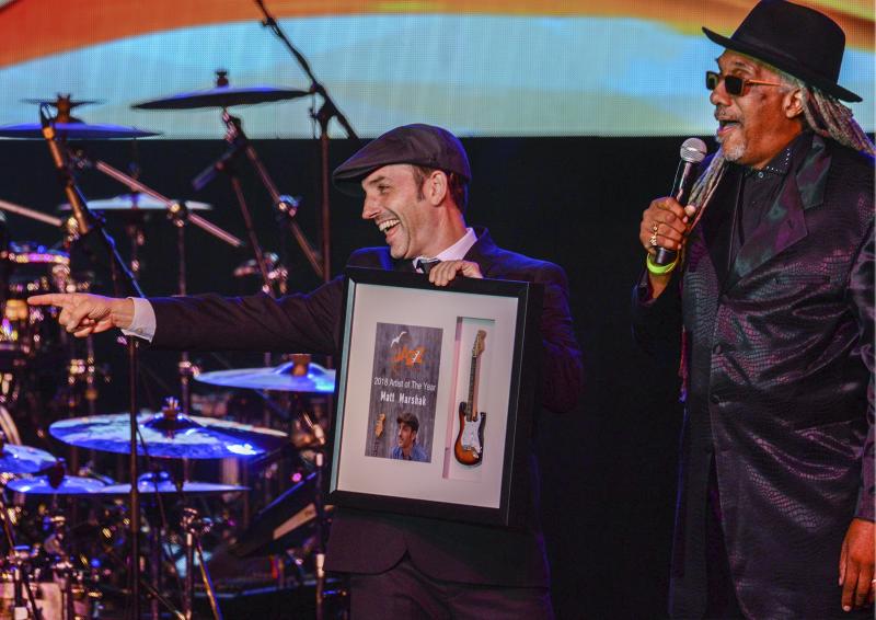 Matt Marshak, Artist of the Year, was recognized Oct. 11 at opening night. “Nine years ago I was afforded the opportunity to be an aspiring new artist. I appreciate them allowing me to grow and learn,” said Marshak. Jazz fest Emcee Perky Scott, right, tells a story about Marshak. DENY HOWETH PHOTO
