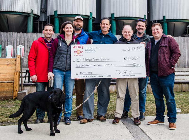 Check presentation attendees shown are (l-r) Sean McGonegal, Urban Bike Project program manager; Laura Wilburn, Urban Bike Project executive director; Mark Carter, Dogfish Head Beer & Benevolence director; Sam Calagione, Dogfish Head founder and CEO; Ryan Kennedy, Movies on Tap, Harvey, Hanna & Associates Inc. vice president of marketing; Jim Miller, Movies on Tap, Out & About Magazine director of publications; and Drew Sheaffer, Movies on Tap/Penn Cinema director of operations. In front is Sam Calagione’s lovable pup Moxie. SUBMITTED PHOTO