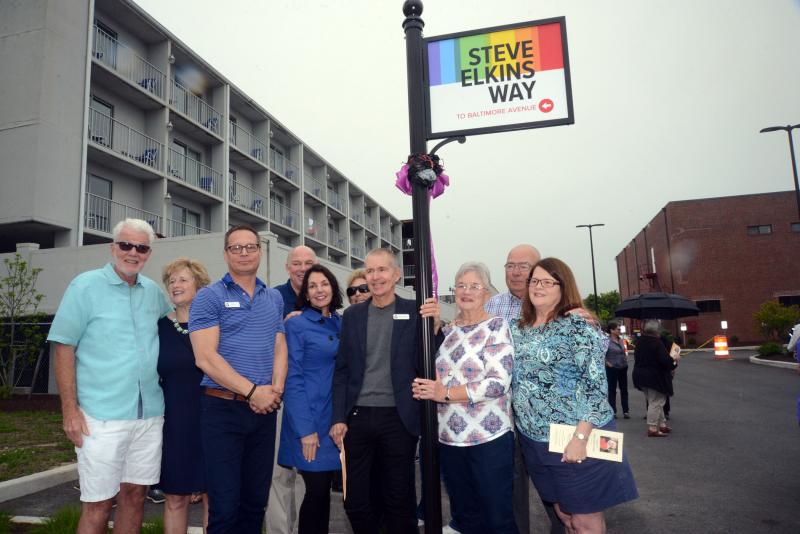 Speakers, friends, family and officials gather under the Steve Elkins Way sign after the unveiling. Shown are (l-r) Rehoboth Commissioners Dick Byrne and Lisa Schlosser, CAMP Rehoboth President Chris Beagle, Rep. Pete Schwartzkopf, State Auditor Kathy McGuiness, Letters from CAMP Rehoboth Editor Fay Jacobs, CAMP Rehoboth Executive Director Murray Archibald, Elkins’ sister Judy Buchanan, Butch Buchanan, and CAMP Rehoboth Administrative Coordinator Monica Parr. STEVEN BILLUPS PHOTOS Steve Elkins Way