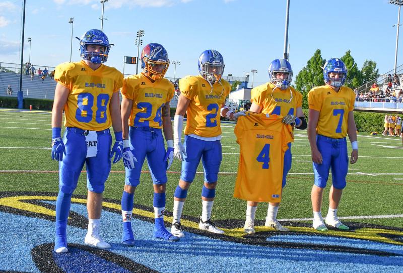 Gold captains Ryan Fields of Middletown, Isaiah Barnes of Sussex Central, Gabe Wescott of Woodbridge, Brock Keeler of Woodbridge and Drew Fry of Middletown holds up Troy Haynes’ jersey during the coin toss. Haynes is undergoing treatment for kidney cancer.