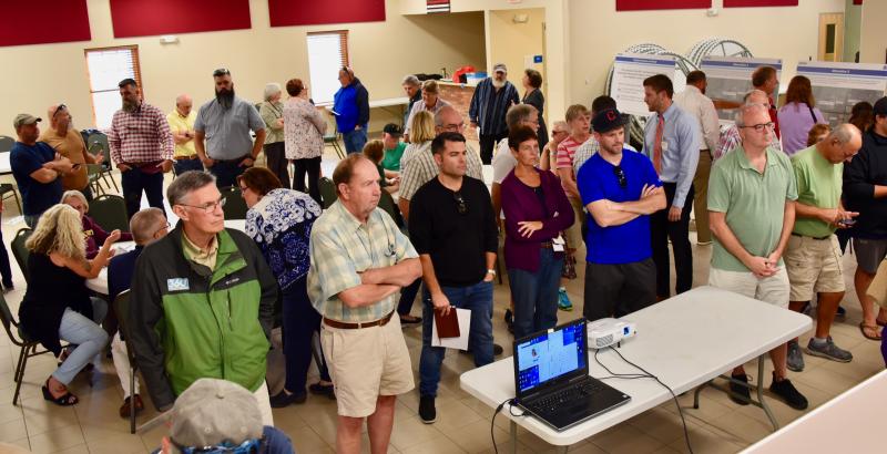 A large crowd watches a simulated video of the alternatives proposed for road improvements at the Cave Neck Road-Route 1 intersection.