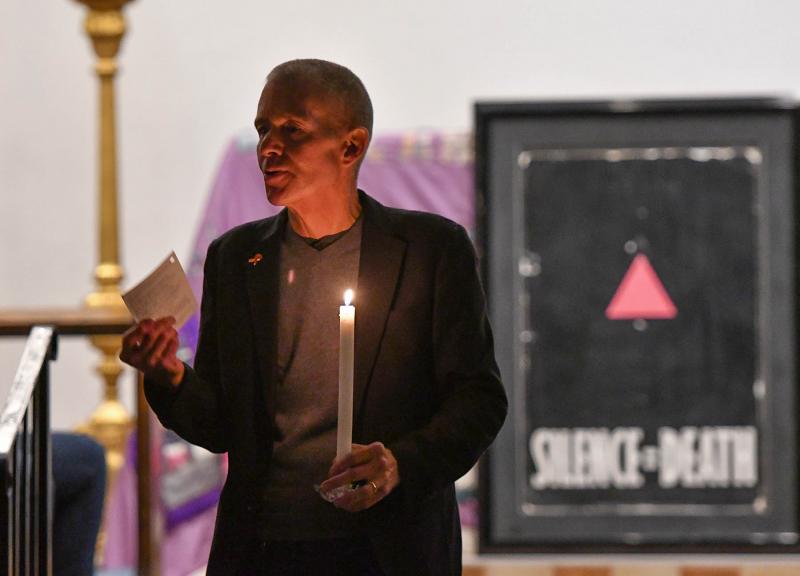 CAMP Rehoboth founder Murray Archibald welcomes all to the service. He stands with the primary slogan of Act-Up. AIDS Coalition to Unleash Power (ACT UP) is an international, grassroots political group working to end the AIDS pandemic. The group works to improve the lives of people with AIDS through direct action, medical research, treatment and advocacy, and working to change legislation and public policies.