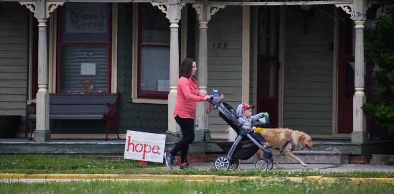 A family takes a walk by a HOPE sign placed in front of Ogre’s Grove in downtown Milton.