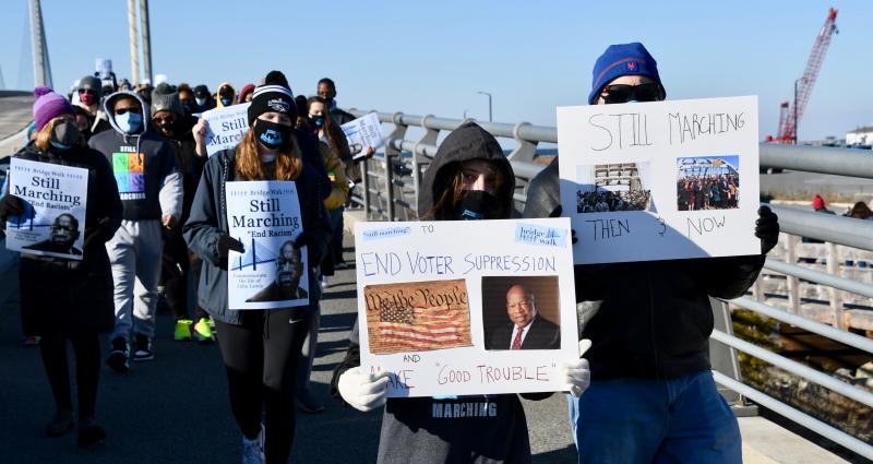 Two walkers hold up handmade signs urging an end to voter suppression. The reference to “Good Trouble” is from a quote by the late John Lewis, who urged those who saw something that wasn’t right or fair to say something and “Get in trouble. Good trouble. Necessary trouble.”