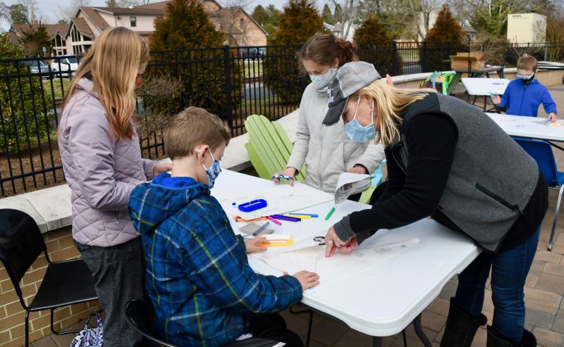 With help from mom Tiffany Kollar, far left, Rachel Webster of Rehoboth Toy & Kite uses a punch to put string holes in the kites of Logan and Adrianna Kollar.