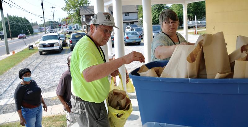 Volunteers Phil Troyer and Greta Browning distribute food and utensil bags to accompany the Thursday-night dinner.