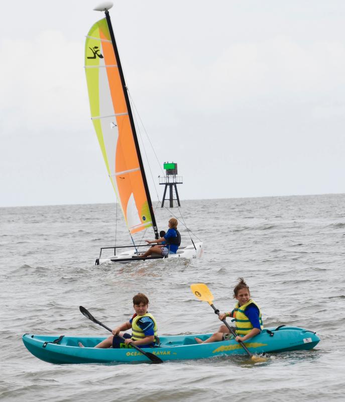 Kayakers Gray Ostrovsky and Jack Comegys paddle parallel to the shore as a Hobie Cat sets sail into Delaware Bay.