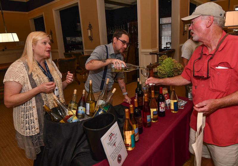 Peggy Raley-Ward of Nassau Valley Vineyards, left, gives information to Rick Gardner as tasting room manager Wes Patton pours his vino.