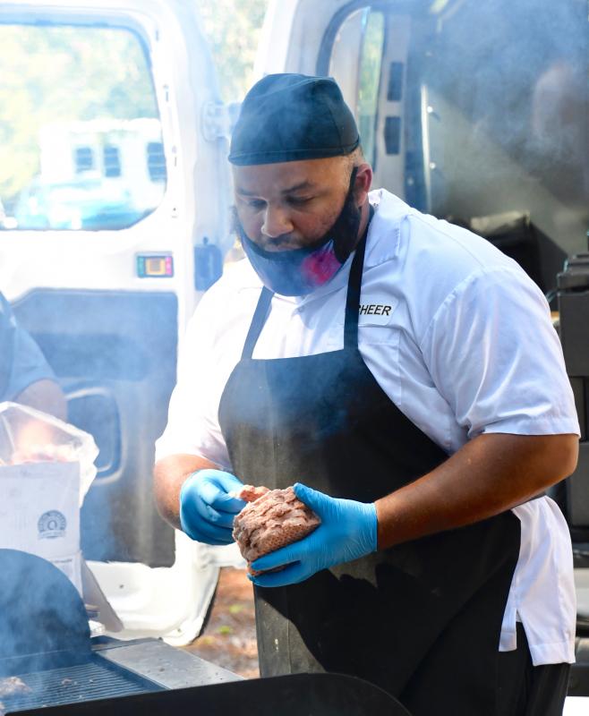CHEER cook Kevin Wilcox is enveloped by smoke from the grill as he prepares hot dogs and hamburgers.
