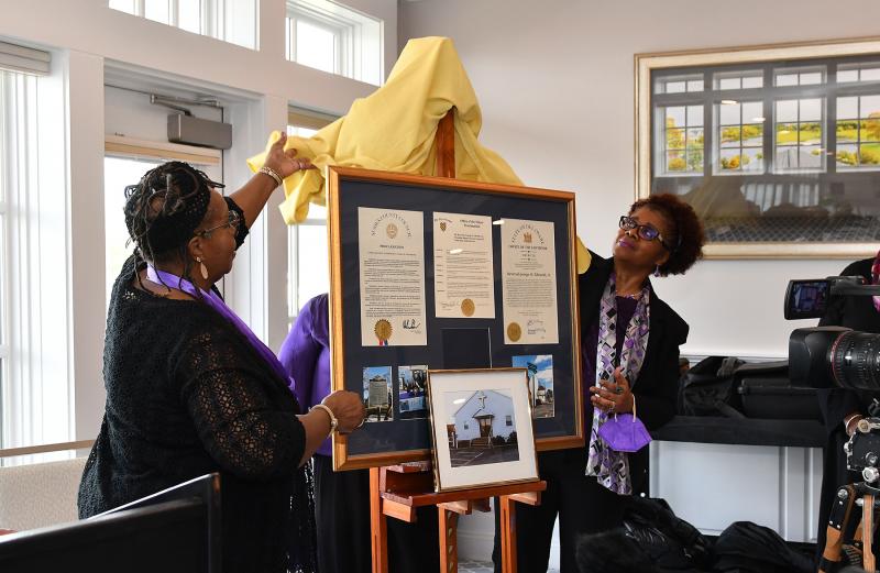 Mistress of Ceremonies Hattie Bull and Trina Brown-Hicks of the Community Celebration Committee unveil the proclamations and photos for the Rev. George Edwards.