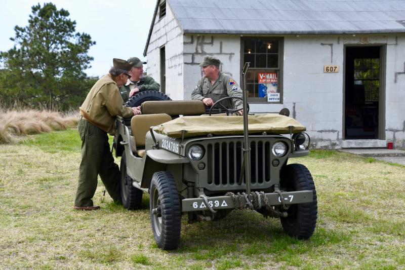In a scene that could be from a photograph taken in the early 1940s at Fort Miles, re-enactors talk shop around an Army Jeep.