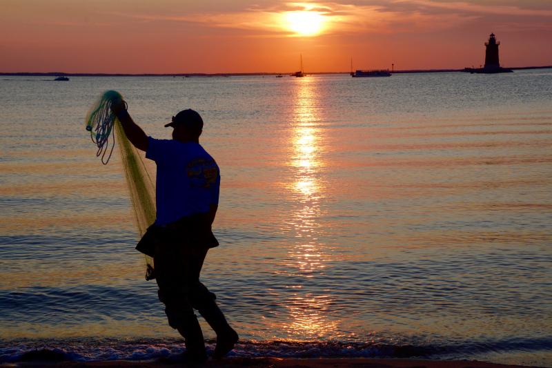 At the end of the day, a fisherman casts his net to catch bait fish along the bay beach in the park.