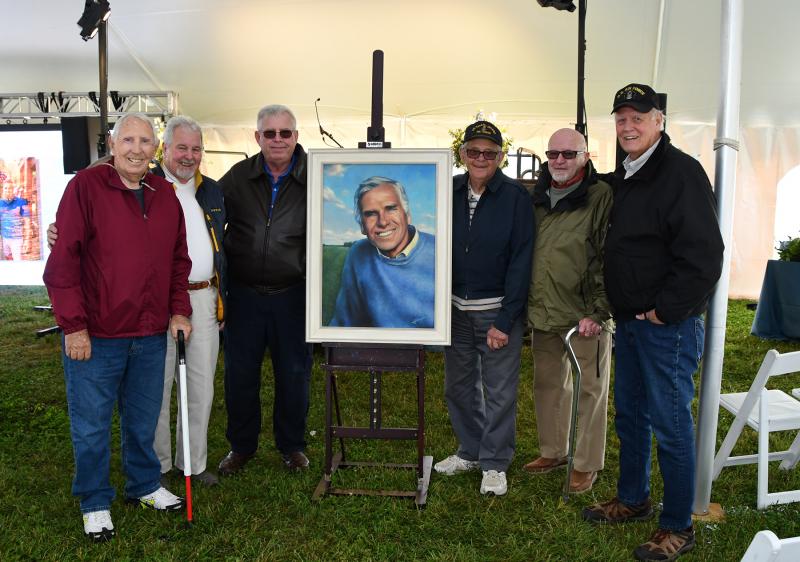 “The guys” gather with Joe Hudson’s portrait. A consummate storyteller, in his older years Joe held court at Surf Bagel and Arby’s with this group of his friends. Shown with Joe’s portrait are (l-r) Dick “Sharpie” Sharp, John Mavromatis, Bill Lankford, Warren Walls, Bob Nicholson and Jeff Mitchell.