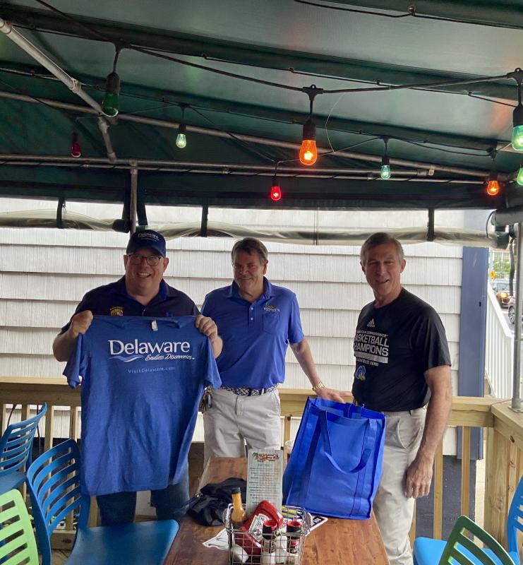 Maryland Gov. Larry Hogan holds up his Delaware-themed gifts while Woody’s Dewey Beach owner Jimmy O’Conor, center, and Gov. John Carney smile.