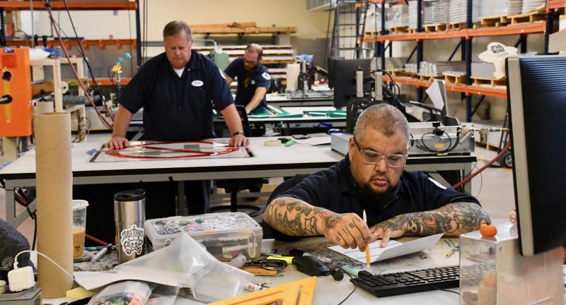 Half of the DelDOT sign-making staff is at work in the Dover shop. The workers are (from back) Scott Hazel, Michael Norland and Bob Brown.