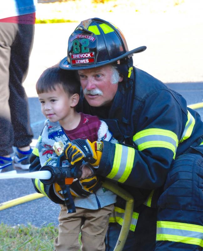 Calvin Dunning, 3, of Rehoboth Beach gets some help from Lewes firefighter Steve Shevock as he uses a fire hose.