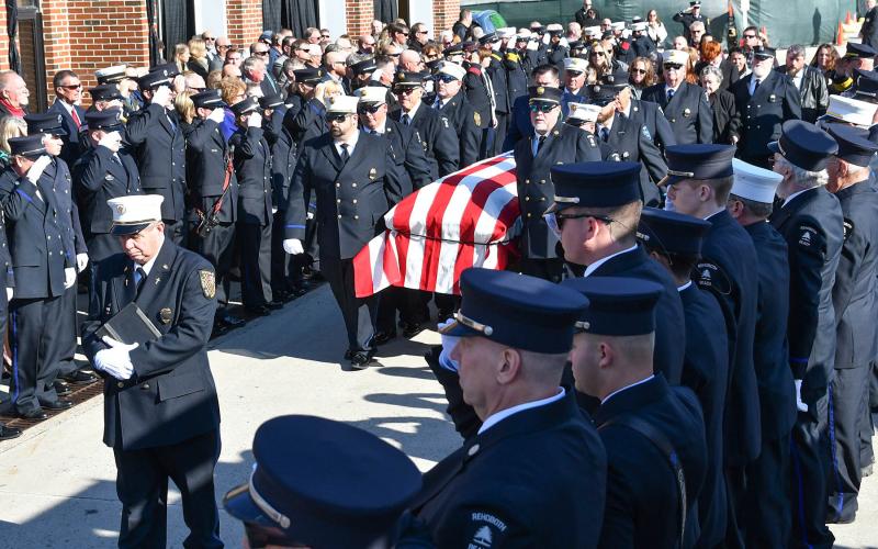 Lewes Fire Department Chaplain Charlie Arnold leads the flag-covered casket among saluting fire department members.