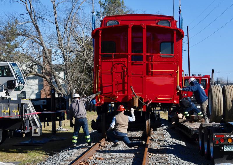 Coastal Towing workers steady the caboose onto the track between the Lewes library and Rollins Community Center in Lewes.
