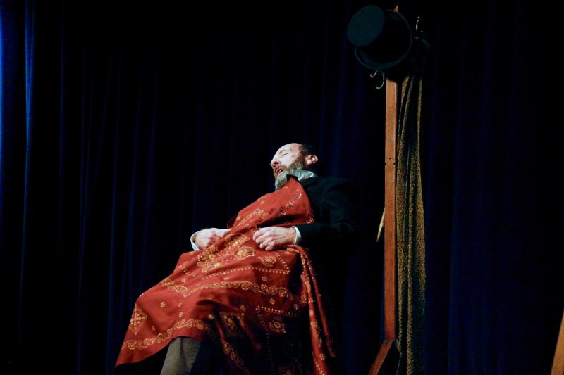 Gerald Dickens made excellent work of his limited props. Scrooge is seen dozing off for the night, fully clothed, of course.