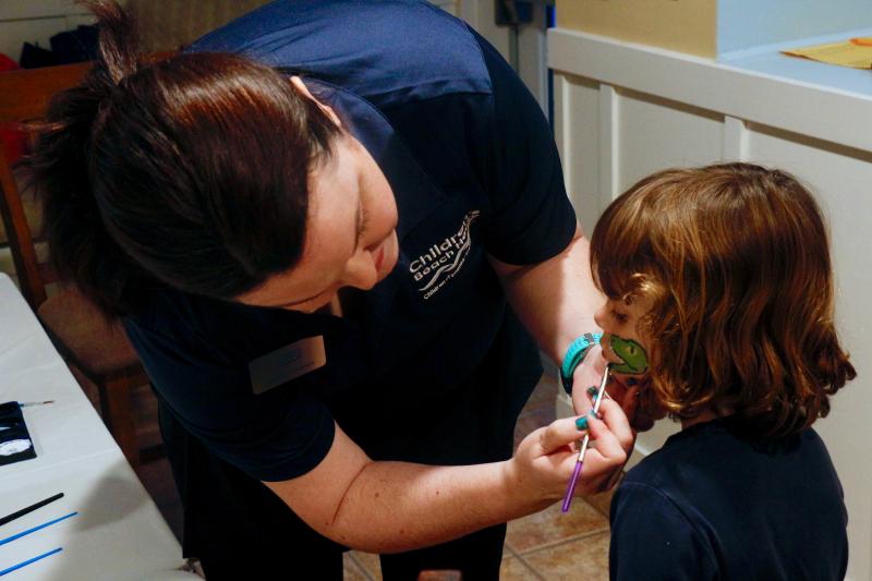 Children’s Beach House teacher Stephanie Federico paints a dinosaur on the cheek of Adrien Kluchnick.