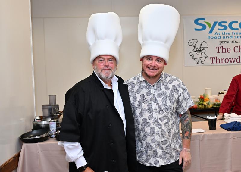 Event emcee Lewis “Drexel” Davison, left, and mystery basket creator and presenter Hari Cameron pose with their giant chef hats, a present from Davison.