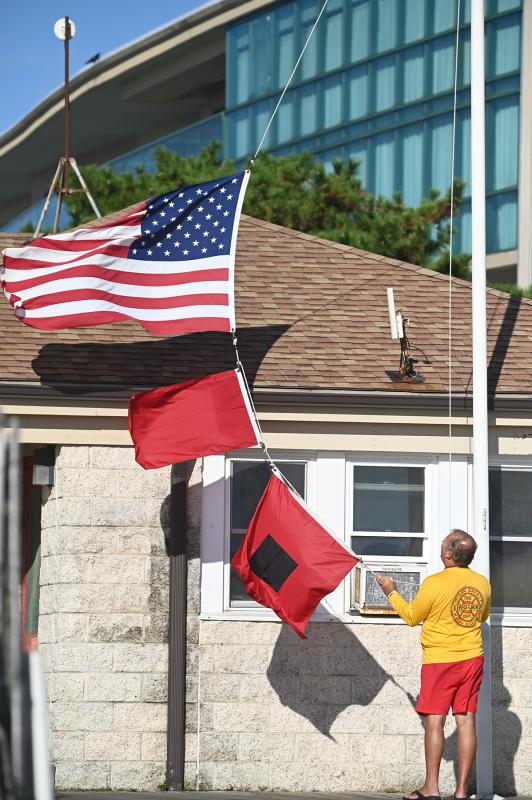 The Rehoboth Beach Patrol has issued a red-flag warning due to surf conditions. The red flag with the black square indicates a storm warning. Hoisting the flags is Chief Rich Szvitich.