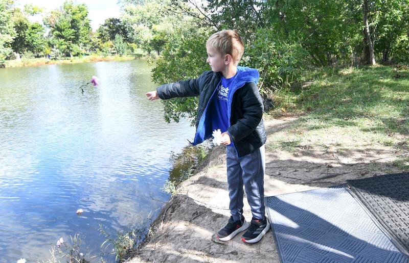Liam Adams tosses a flower into Blockhouse Pond in remembrance of his siblings as a symbol of their lives.