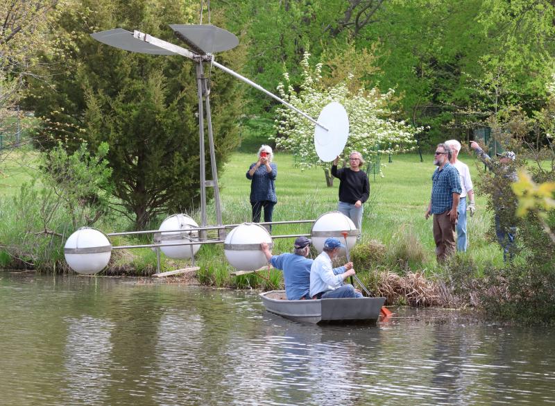 The sculpture, “M.T. Skirt,” is lowered into Blockhouse Pond April 24. Artist Paul Daniel and Steve Walker from the Lewes Public Art Committee are in the boat, helping guide the floating art work into the water. On shore are (l-r), Laurie Walker, Heidi Lowe, Kyle Miller and Tim Ritzert. BILL SHULL PHOTOS