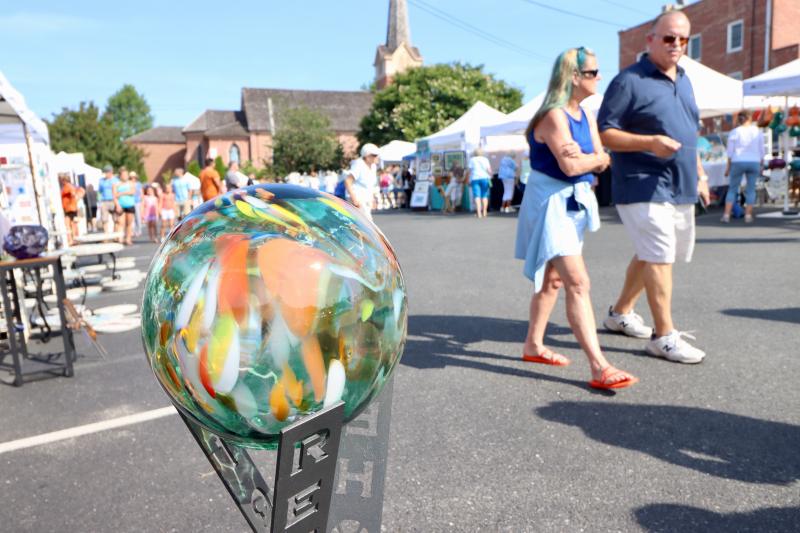 People walk past one of Bud Broda-Knudsen’s glass orbs in front of his booth in the M&T Bank parking lot.