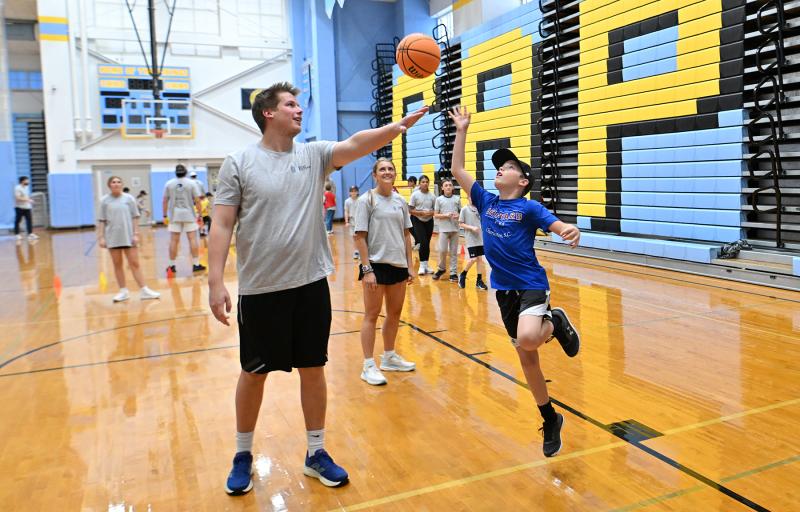 Mason Rogers, 11, goes in for a shot on former Cape all-star and Randolph Macon national champion basketball player Ian Robertson as Northwestern field hockey national champion Alia Marshall looks on.