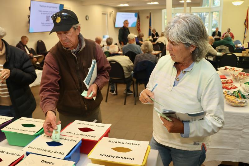 Bill Adelman, left, and Susan Russell deposit their Lewes bucks at the end of the Lewes Citizen Engagement Workshop Nov. 21. The workshop was an exercise to get input on budget priorities. People used the fake money to fill bins representing taxes and fees they would be willing to see increased. BILL SHULL PHOTOS