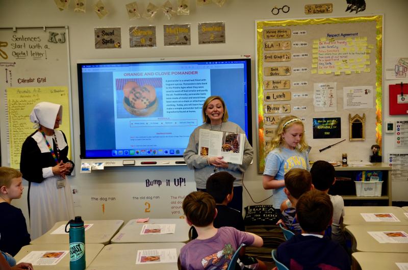 Dressed for the occasion, Stacy Kotch-Jester, left, listens to Brittany Hoelle explain how students will make orange and clove pomanders as Vivian Hoeller shows her classmates examples.