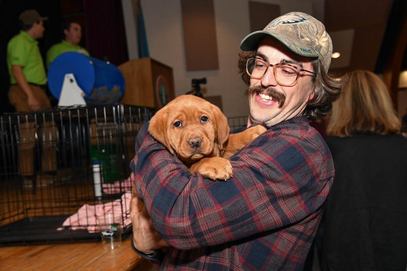 Volunteer Charlie Burton holds the red fox lab that was won by Alexander Lombardo with a winning bid of $5,000.