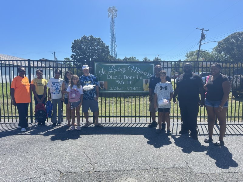 Event attendees stand next to the banner honoring West Side New Beginnings co-founder Diaz Bonville. Shown are (l-r) West Side New Beginnings co-founder Brenda Milbourne, Nyla Alford, Kayla Alford, Josi Kime, Olivia Kime, Bob Kime, Cape Henlopen school board member Bill Collick, Dom Kime, Shayne Brittingham and Brianna Jones. SUBMITTED PHOTO