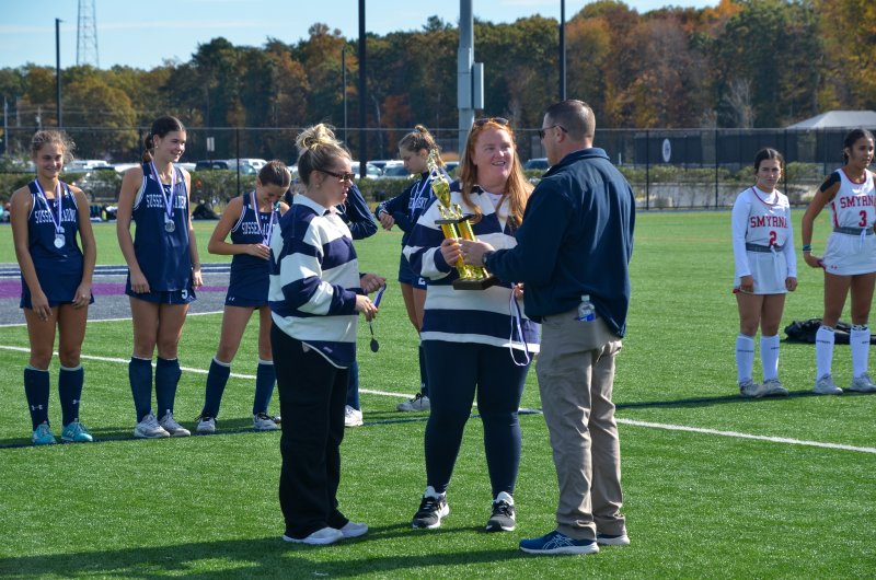 Sussex Academy coach, and Cape grad, Caitlyn Hardy accepts the Henlopen South trophy with coach Lexie Thomas from Cape Assistant Athletic Director Michael Connors.