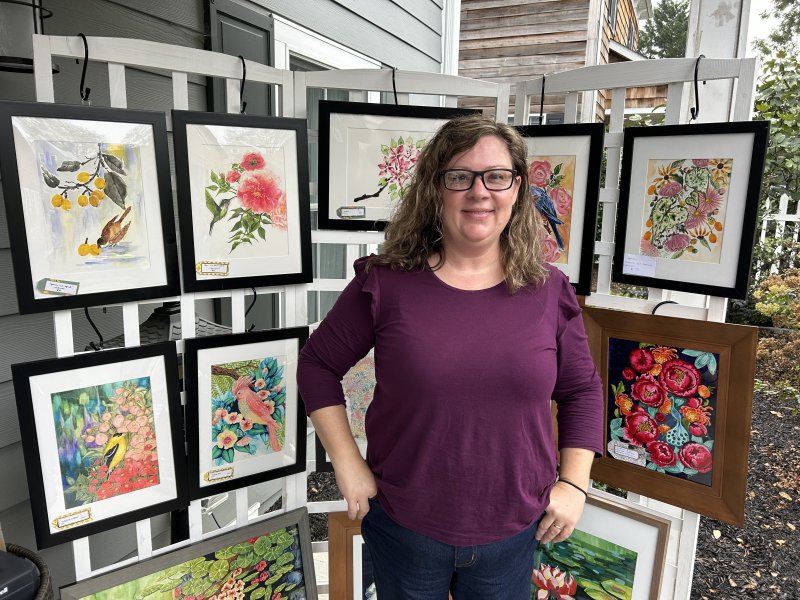 Jessica Critchlow stands in front of her paintings, with her works also including ornaments and painted pumpkins.
