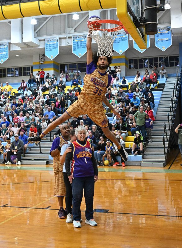 Harlem Wizard star Sky-Rise aka Tyler Cronk, flies through the air and slams a dunk over legendary teammate A-Train, Beacon Middle School counselor Elizabeth Luff and Gail Dejmal from the Rotary Club.